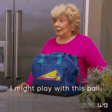 a woman in a pink sweater is holding a blue bag that says i might play with this ball