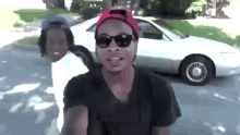 a man wearing sunglasses and a pink hat is standing in front of a white car