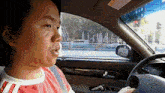 a man in a red shirt is driving a silver car