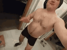 a man without a shirt is taking a selfie in a hallway .