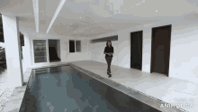 a woman is standing next to a large swimming pool in an empty house
