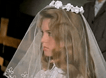 a little girl in a wedding dress and veil is looking at the camera .