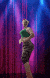 a woman in a green top is dancing on a stage in front of a pink curtain