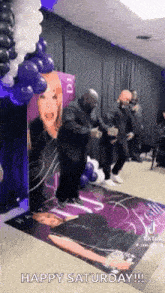 a group of men are dancing in a room with balloons and a picture of a woman on the wall .