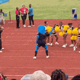 a mascot is dancing on a track with cheerleaders in the background .