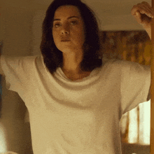 a woman wearing a white t-shirt is standing in front of a window