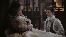 a woman is holding a baby in her arms while another woman looks on .