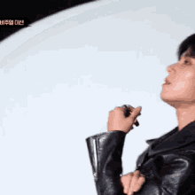 a man in a black leather jacket is standing in front of a white wall holding a pen .