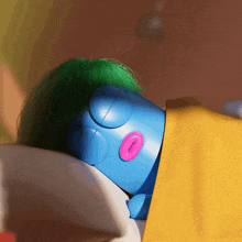 a blue toy with green hair and a pink nose is sleeping on a bed