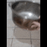 a person is pouring water into a metal bowl on a tiled floor .