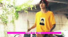 a man wearing a yellow t-shirt with a picture of a boy on it is standing next to a car .