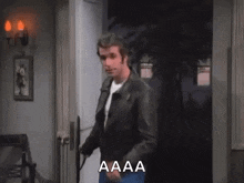 a man in a leather jacket is standing in front of a door and holding a gun .