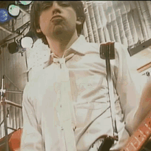 a man in a white shirt and tie plays a guitar