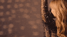 a woman in a gold sequined dress is dancing with her arms in the air .