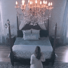 a woman stands in front of a bed with a chandelier hanging over it