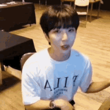 a young man wearing a white t-shirt is sitting at a table with his arms outstretched .