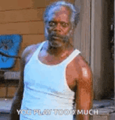 a man in a white tank top is standing in front of a door and looking at the camera .