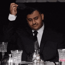 a man in a black suit and tie is sitting at a table