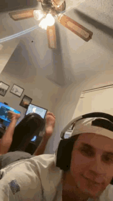 a man wearing headphones is taking a selfie in a living room with a ceiling fan behind him .