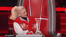 a woman in a red jacket is sitting in a chair with a nbc logo on the back