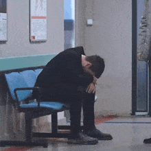 a man is sitting on a blue bench with his head down .
