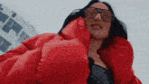 a woman wearing a red jacket and sunglasses is looking down at the camera .