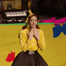 a woman in a yellow shirt and black skirt is standing in front of a piano