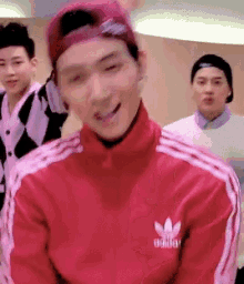 a man wearing a red adidas jacket and a pink hat is smiling