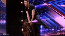 a man is riding a woman on a stage with a nbc logo behind him