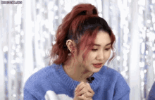 a woman with red hair and a blue sweater is sitting in front of a microphone .