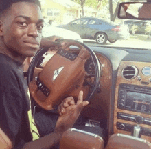 a young man is sitting in the driver 's seat of a bentley car giving the middle finger .