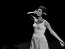 a black and white photo of a woman in a white dress dancing .
