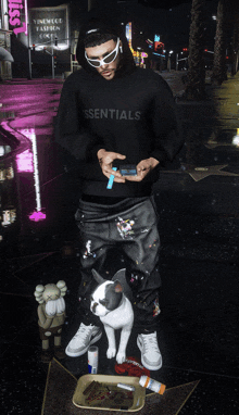 a man wearing a essentials hoodie stands next to a dog