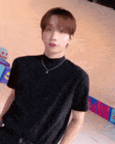 a young man is wearing a black t-shirt and a necklace .