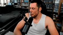 a man wearing a white tank top is talking into a microphone