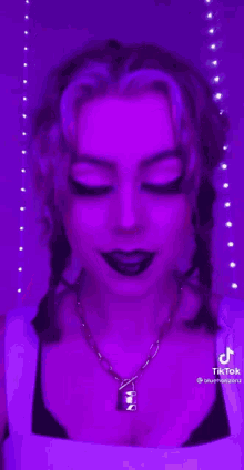 a woman wearing a necklace with a padlock on it is standing in front of a purple wall .