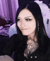 a woman with long black hair and a tattoo on her chest is smiling while sitting in a chair .