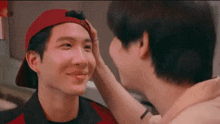 two men are touching each other 's faces while one of them is wearing a red hat .