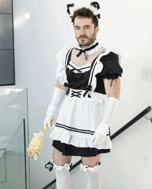 a man dressed in a maid costume holds a yellow duster