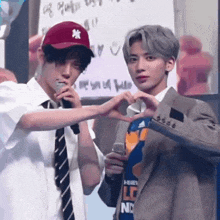 two young men are making a heart shape with their hands while one is wearing a baseball cap