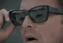 a man wearing sunglasses is taking off his sunglasses and looking at the camera .
