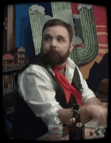 a man with a beard and a red scarf is sitting at a table with a bottle of water