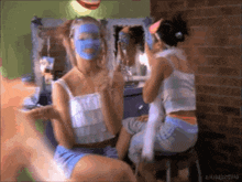 a woman with a blue mask on her face looks at herself in the mirror