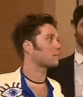 a man in a white jacket with an eye on it is standing next to another man in a blue shirt .