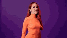 a woman with red hair is wearing a bright orange turtleneck and heart shaped earrings