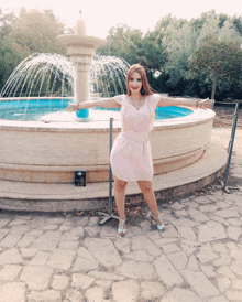 a woman stands in front of a fountain with her arms outstretched