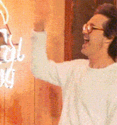 a man wearing glasses and a white shirt stands in front of a neon sign that says ' cool nuts '
