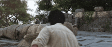 a man in a white shirt is standing in front of a large stone wall