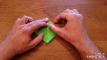 a person 's hands folding a green square with the words made in animotica below