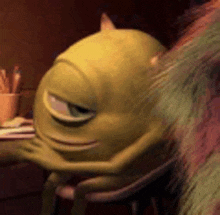 mike wazowski from monsters inc is sitting at a desk with a book .